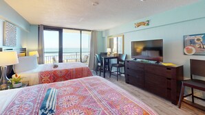 Ein Hotelzimmer mit zwei Betten, einem Schreibtisch, einem Fernseher und einem Balkon mit Blick.