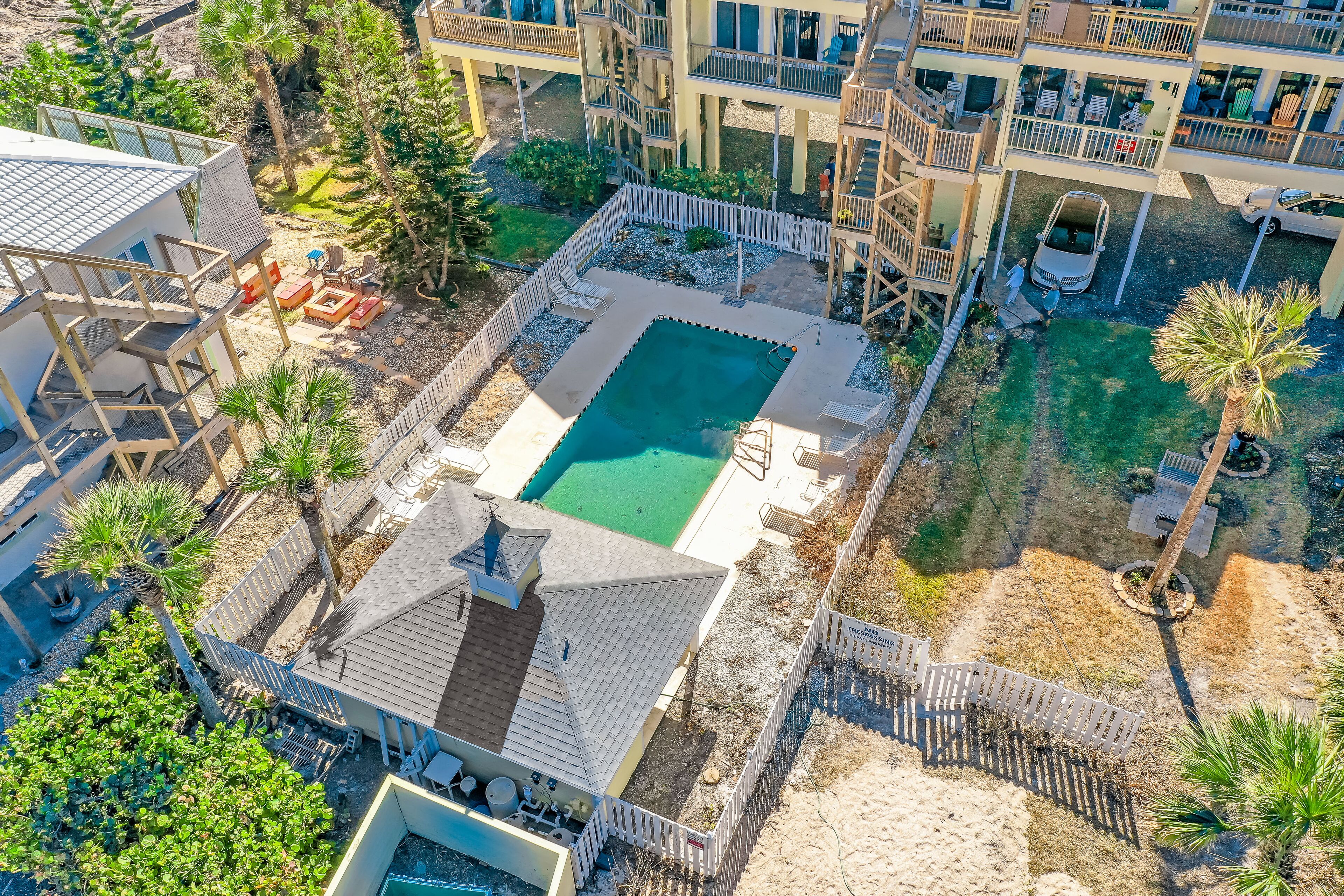An aerial view of a residential area with a swimming pool, multiple balconies, and a fenced yard.