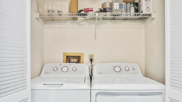A laundry room with two front-loading washing machines, a shelf above with various items, and a small window. - Ormondy A6 - Ocean Shores Getaway (Ormond Beach)