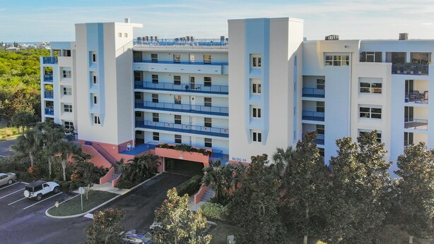 A multi-story hotel with balconies, a parking area, and a landscaped entrance. - Oceanwalk 16-305 (New Smyrna Beach)