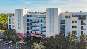 A multi-story hotel with balconies, a parking area, and a landscaped entrance.