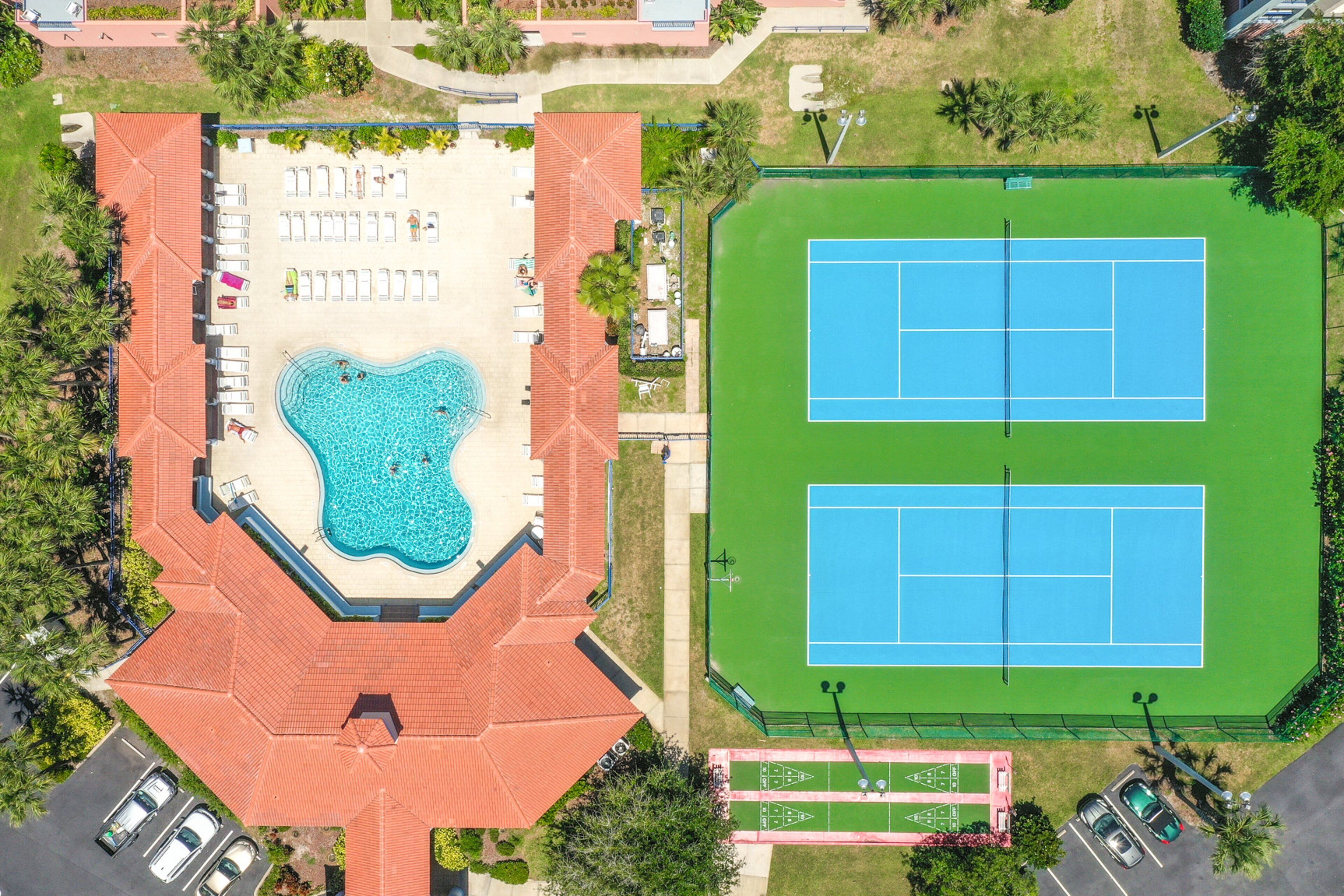 An aerial view of a resort with a swimming pool, tennis courts, and a parking area.