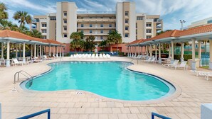 A swimming pool surrounded by lounge chairs and a large hotel building with multiple floors and balconies. - Oceanwalk 16-305 (New Smyrna Beach)
