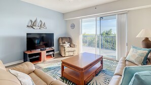 A living room with a sofa, a coffee table, a TV, and a balcony with a railing. - Oceanwalk 16-305 (New Smyrna Beach)
