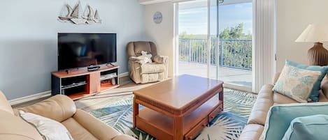 A living room with a sofa, a coffee table, a TV, and a balcony with a railing.