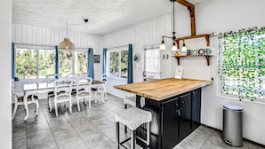 A kitchen with a wooden island, white chairs, and a dining table. - River Cottage (Edgewater)