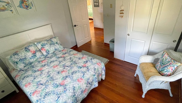 A bedroom with a bed, a chair, and a door leading to another room. - River Cottage (Edgewater)