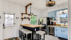 A kitchen with a wooden island, bar stools, a refrigerator, and a sink. - River Cottage (Edgewater)