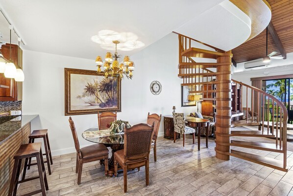 A spacious dining area with a round table and chairs, a chandelier, and a staircase with wooden railings.