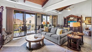 A spacious living area with a large sliding glass door leading to a balcony, a grey sofa, a coffee table, and a wooden sideboard with lamps. - Kamaole Sands 5-414 (Kihei)
