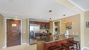A modern kitchen with granite countertops, stainless steel appliances, and wooden bar stools. - Honua Kai Konea 505 (Kaanapali)