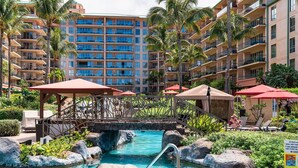 A hotel pool area with a bridge, lounge chairs, and umbrellas. - Honua Kai Konea 505 (Kaanapali)