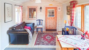 A cozy living room with a sofa, a table with a tablecloth, a rug, a wooden door, and a window with curtains.