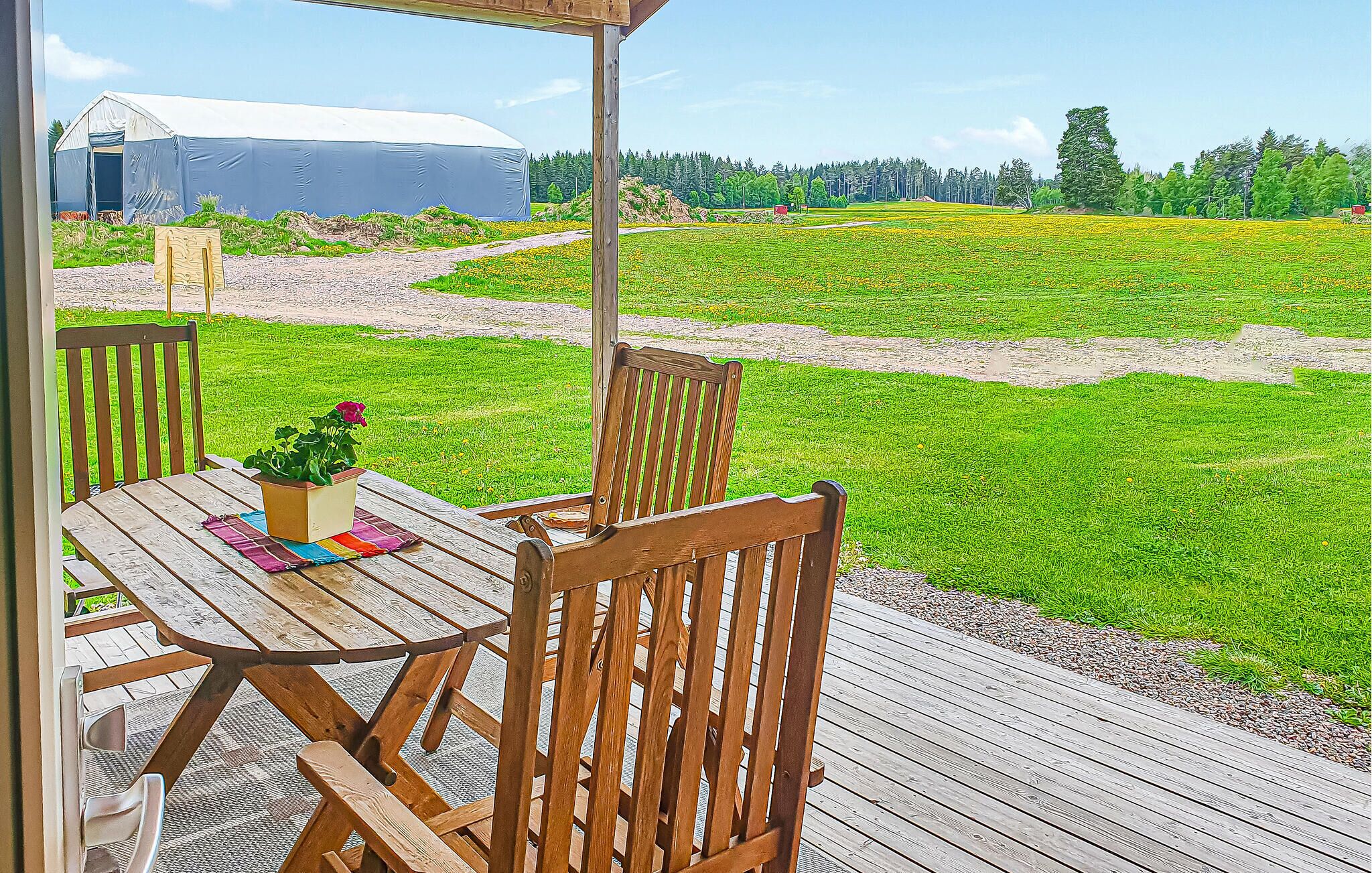 Un espace extérieur aménagé avec des chaises et une table en bois, offrant une vue sur un champ avec une grange en arrière-plan.