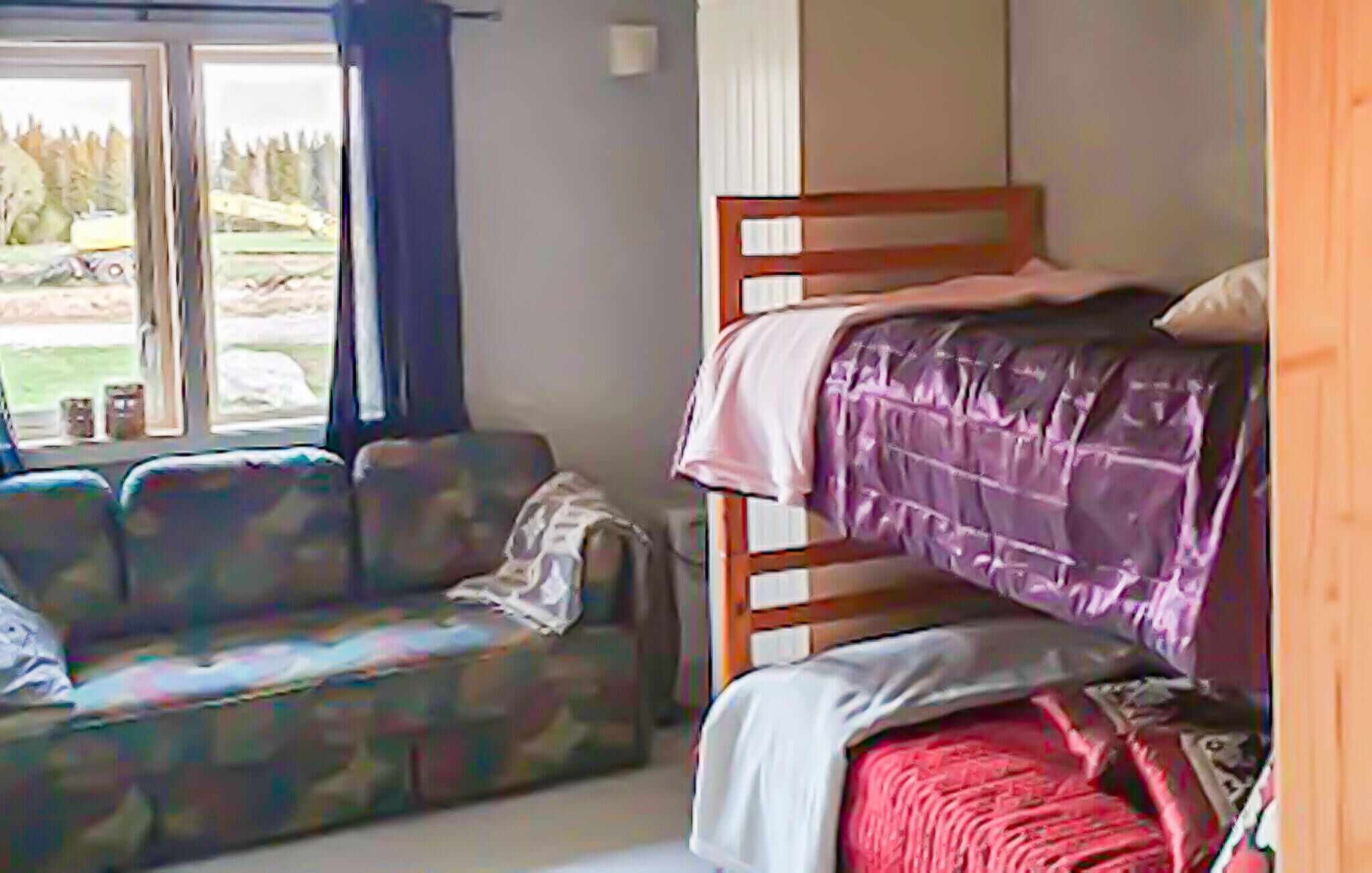 A room with a bunk bed, a couch, and a window with a view of trees and a vehicle outside.