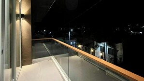 A modern balcony with glass railings and a wooden floor, overlooking a cityscape at night. - Luxury Villa with Private Pool for Gathering near Davao Airport (Davao)