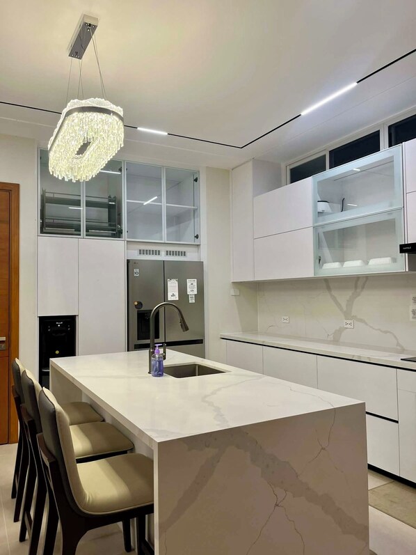 A modern kitchen with a marble island, built-in appliances, and a pendant light.