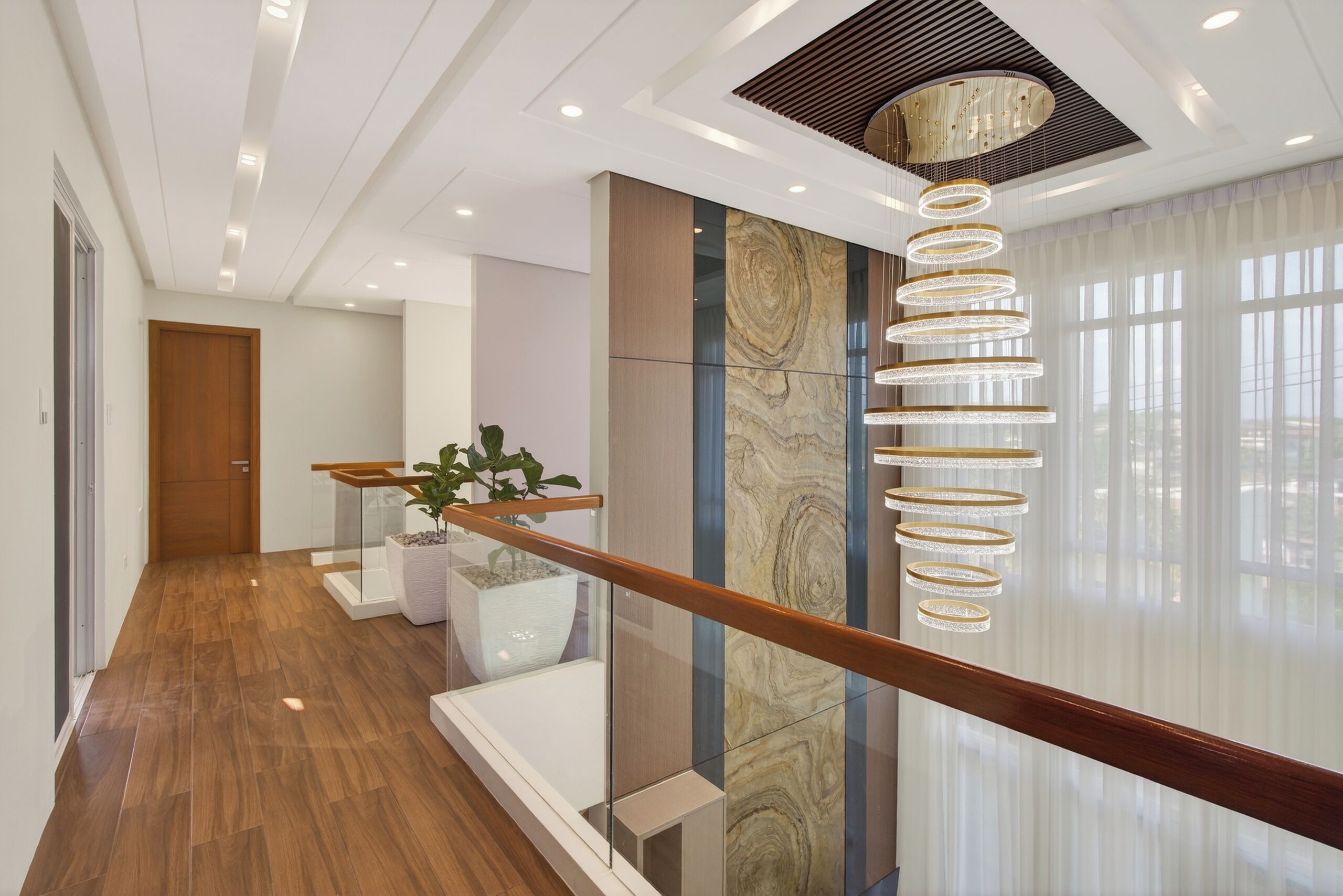 A modern interior with a wooden floor, a glass railing, and a decorative light fixture.