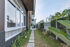 A narrow pathway leading to a modern house with large windows and a well-maintained garden.