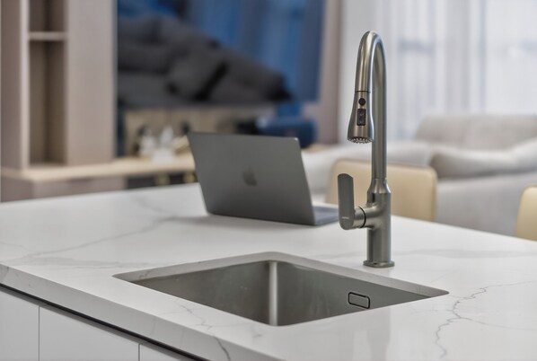 A modern kitchen with a stainless steel sink, a laptop on the counter, and a sofa in the background. - Luxury Villa with Private Pool for Gathering near Davao Airport (Davao)