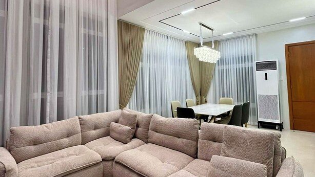 A modern living room with a large sectional sofa, a dining area with a table and chairs, and a large window with sheer curtains. - Luxury Villa with Private Pool for Gathering near Davao Airport (Davao)