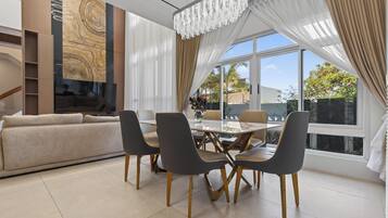 A modern dining area with a chandelier, a sofa, and a view of the outdoors.