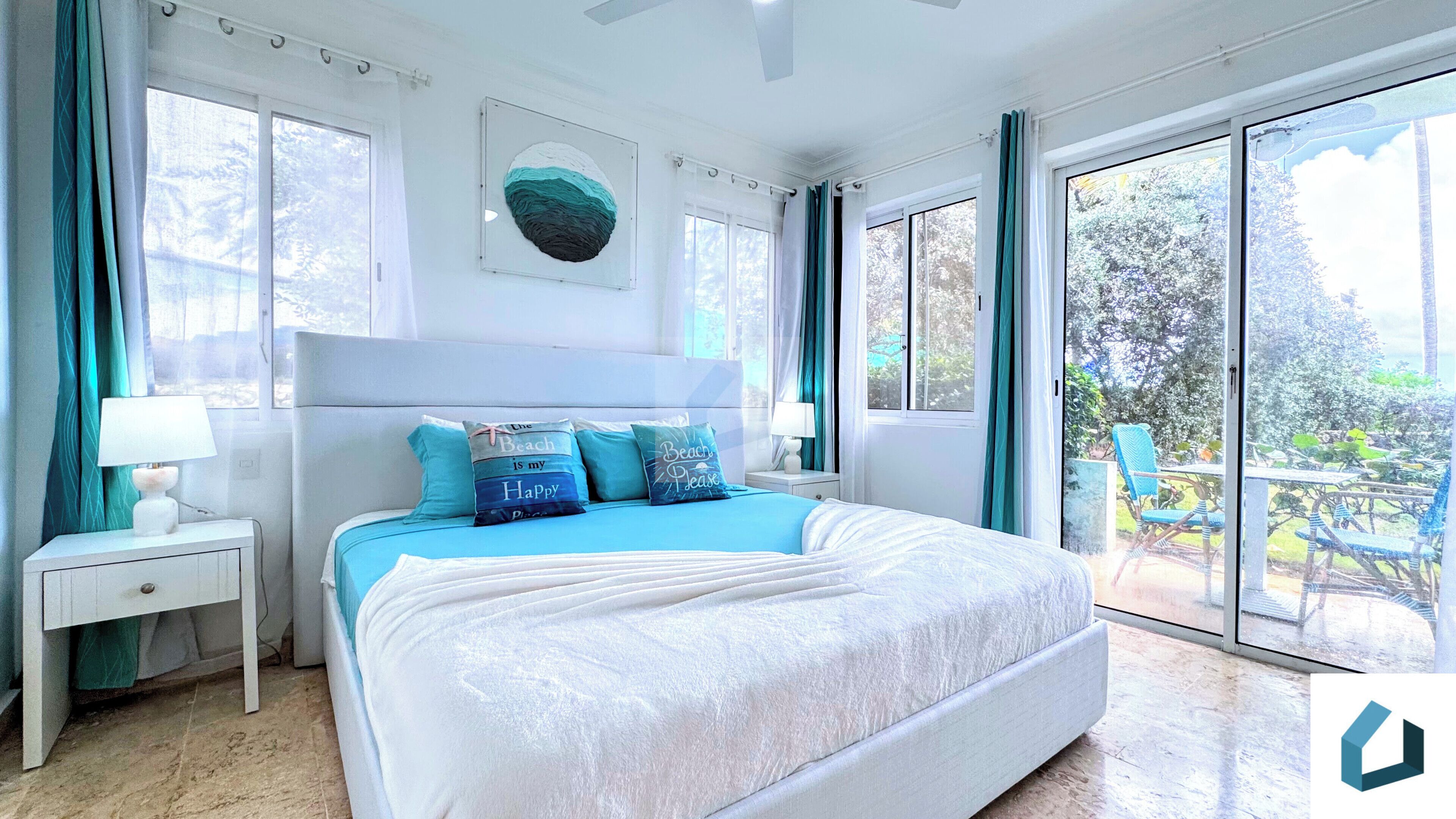 A bedroom with a large bed, two bedside tables with lamps, a window with curtains, and a view of the outdoors.