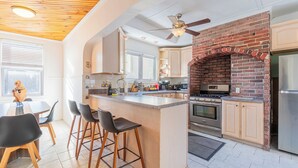 A modern kitchen with a central island, bar stools, a brick oven, and stainless steel appliances. - Cozy 3Bed only 4min from tufts-10min from downtown Boston (Medford)