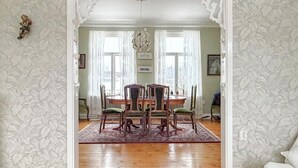 Een eetkamer met een houten tafel en stoelen, een kamerkleed met dessin en een kroonluchter.
