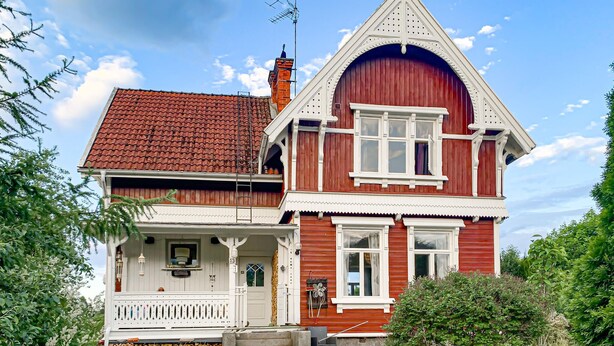 Een tweelaags huis met een rode gevel, witte details en een pannendak.