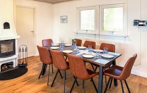 A dining area with a table set for six, surrounded by six chairs, a fireplace, and two windows.