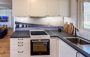 A compact kitchen with a stove, oven, and sink, a wooden dining table, and a view of a bridge through a window.