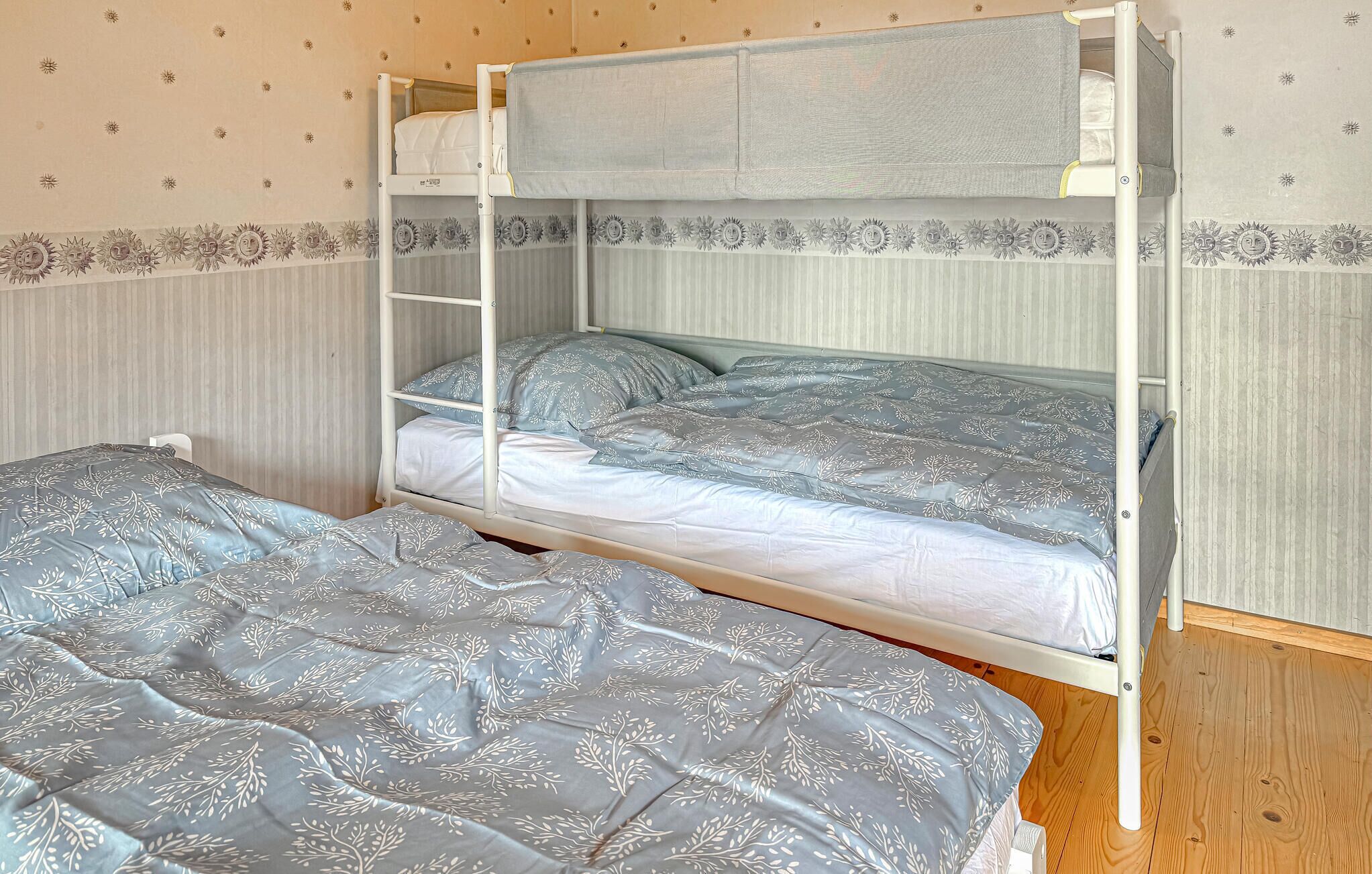Una cama litera con una escalera, dos camas con ropa de cama de diseño floral y una pared con un dibujo de sol.