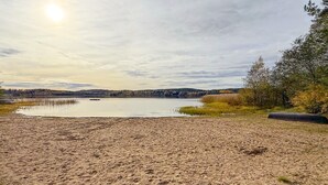 Ein sandiger Strand mit einem ruhigen See, Bäumen und einer entfernten Hügelkette.