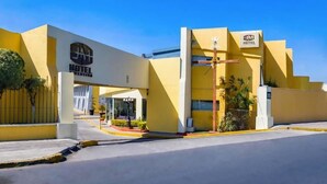 Entrada de un hotel con fachada amarilla y un llamativo letrero que dice 'JM Hotel', bajo un cielo despejado.