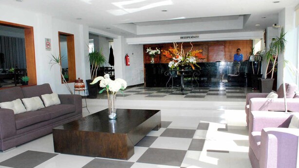 Un vestíbulo de hotel con suelo a cuadros, sofás, un mostrador de recepción y un recepcionista.