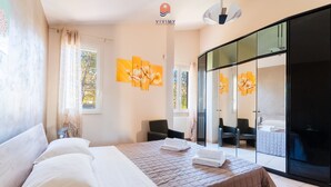 Hotellihuone, jossa on sänky, tuoli, sohva ja liukuovet, jotka johtavat parvekkeelle.