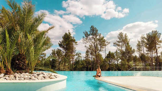 A swimming pool with a person sitting on the edge, surrounded by trees and rocks. - Holiday home with terrace (Tar/Poreč)