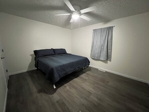 A bedroom with a bed, a ceiling fan, and a window with curtains.
