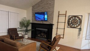 A living room with a fireplace, a mounted TV, a clock, and two armchairs. - Serene 3-bedroom townhome in welcoming Evanston perfect for relaxing. (Evanston)