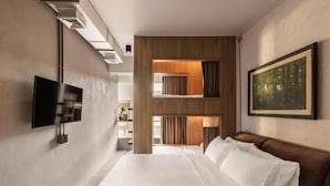 Ein modernes Hotelzimmer mit einem großen Bett, einem Flachbildfernseher, einem Gemälde und Blick ins Freie.