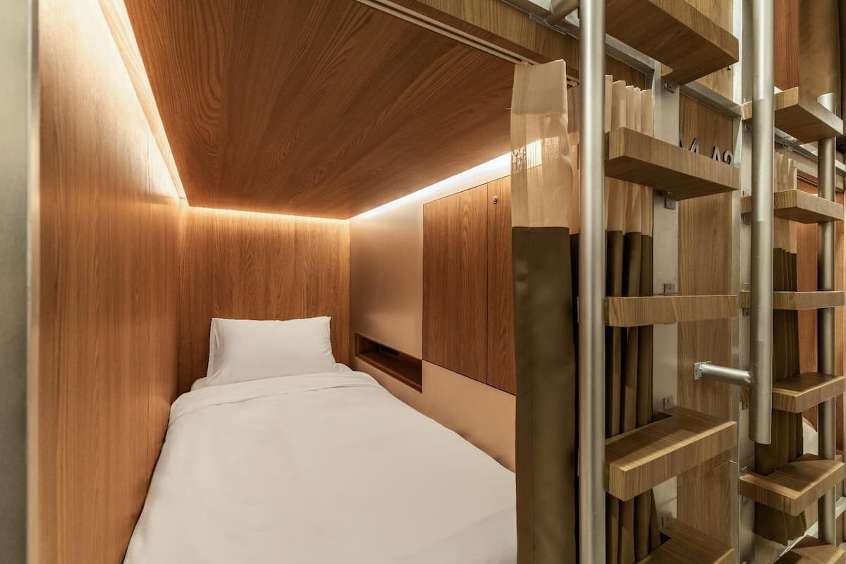 Een moderne hotelkamer met een houten hoofdeinde, een bed met wit beddengoed en ingebouwde houten planken.
