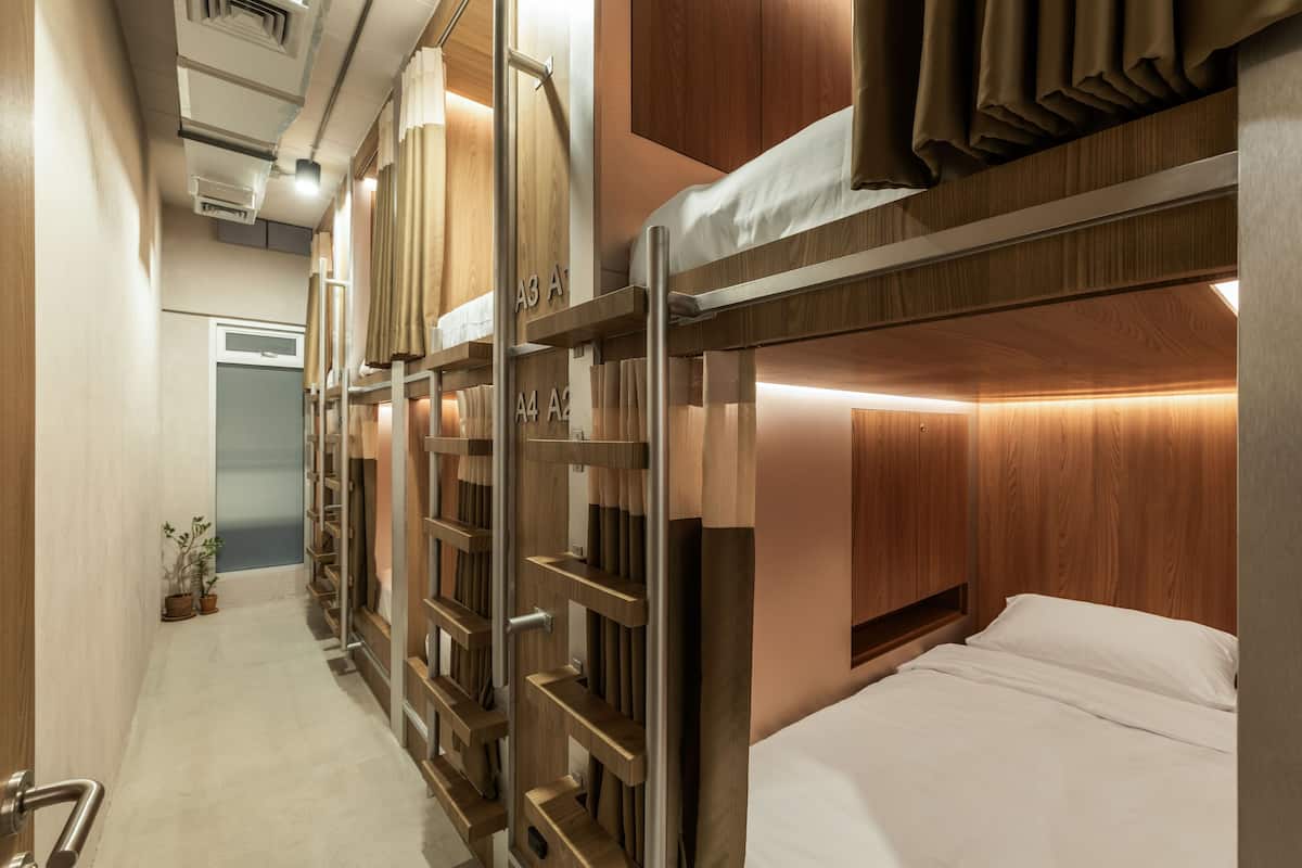 Een slaapkamer met een stapelbed, een houten hoofdbord, een klein nachtkastje en een pot met een plant.