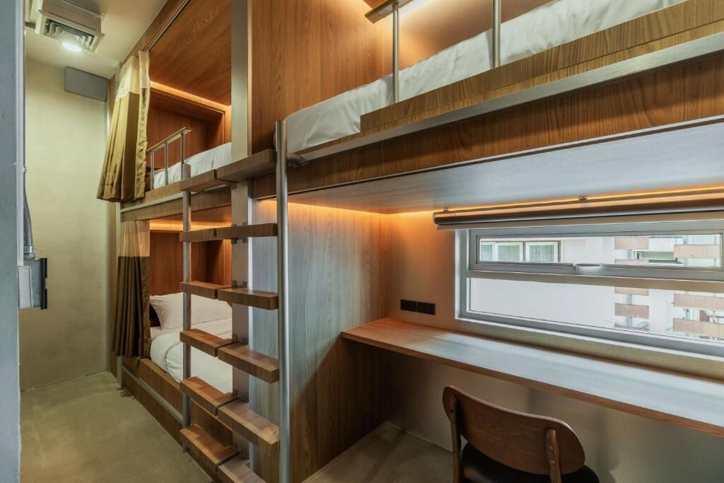 A bunk bed room with a desk and chair, a window with a view, and a wooden wall.