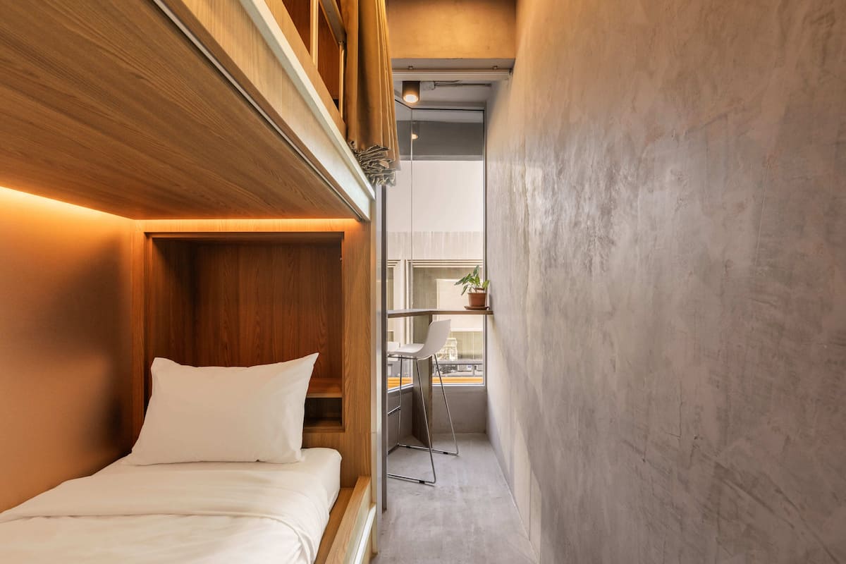 Een smalle hotelkamer met een bed, een klein bureau en een raam.