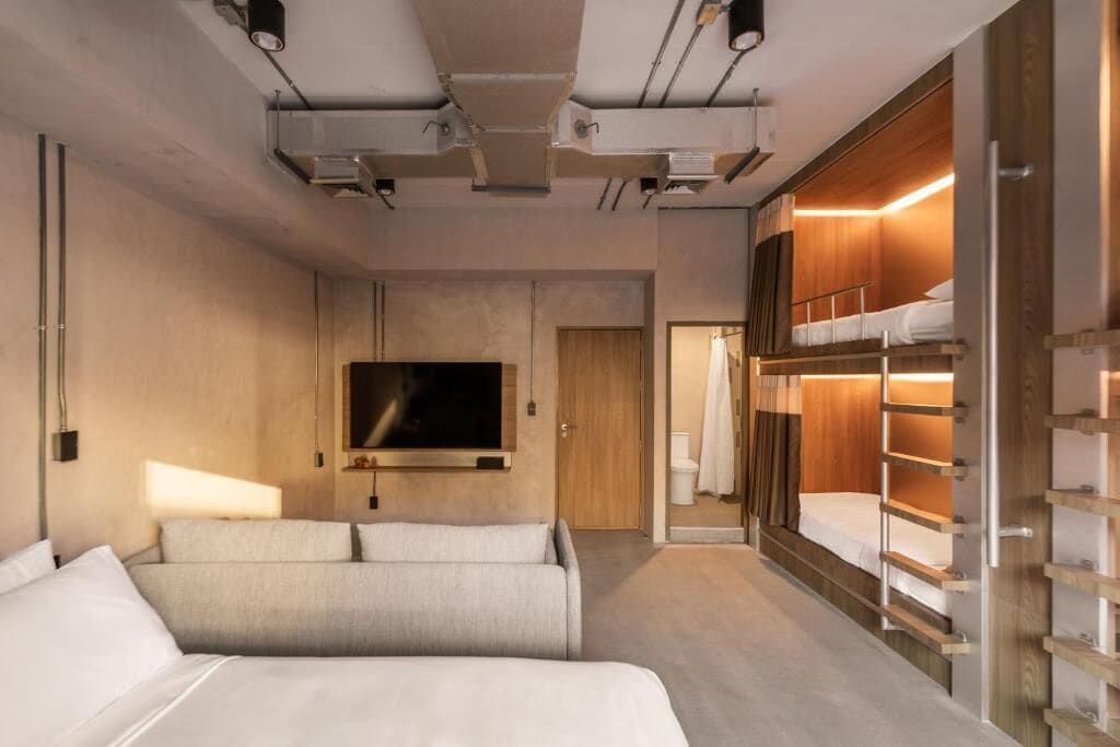 A modern hotel room with a large bed, a TV, a wardrobe, and a bunk bed.