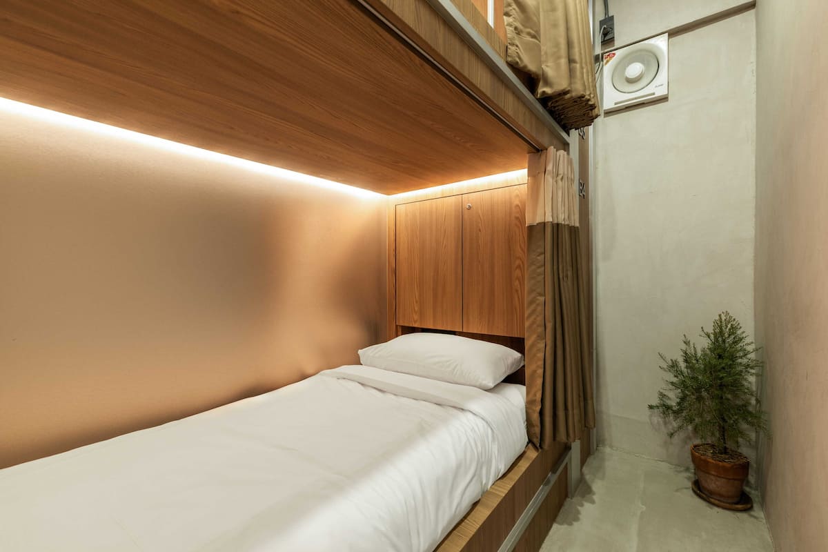 Een kleine slaapkamer met een enkel bed, houten hoofdbord en een kamerplant.