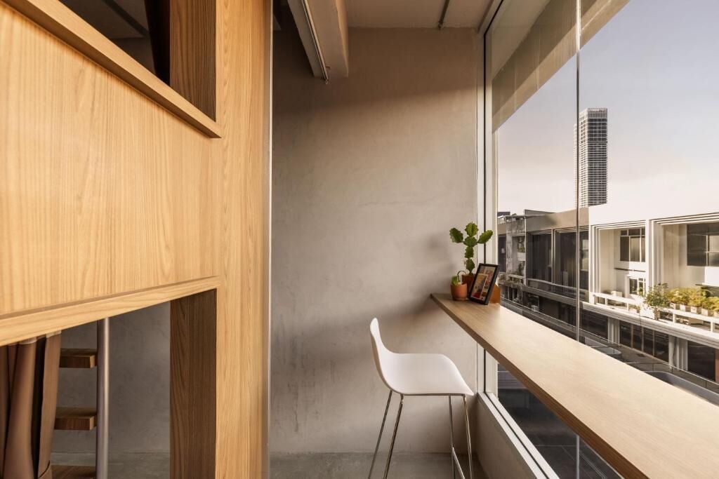 A modern interior with a wooden panel wall, a white chair, a small table with a plant, and a view of buildings through large windows.