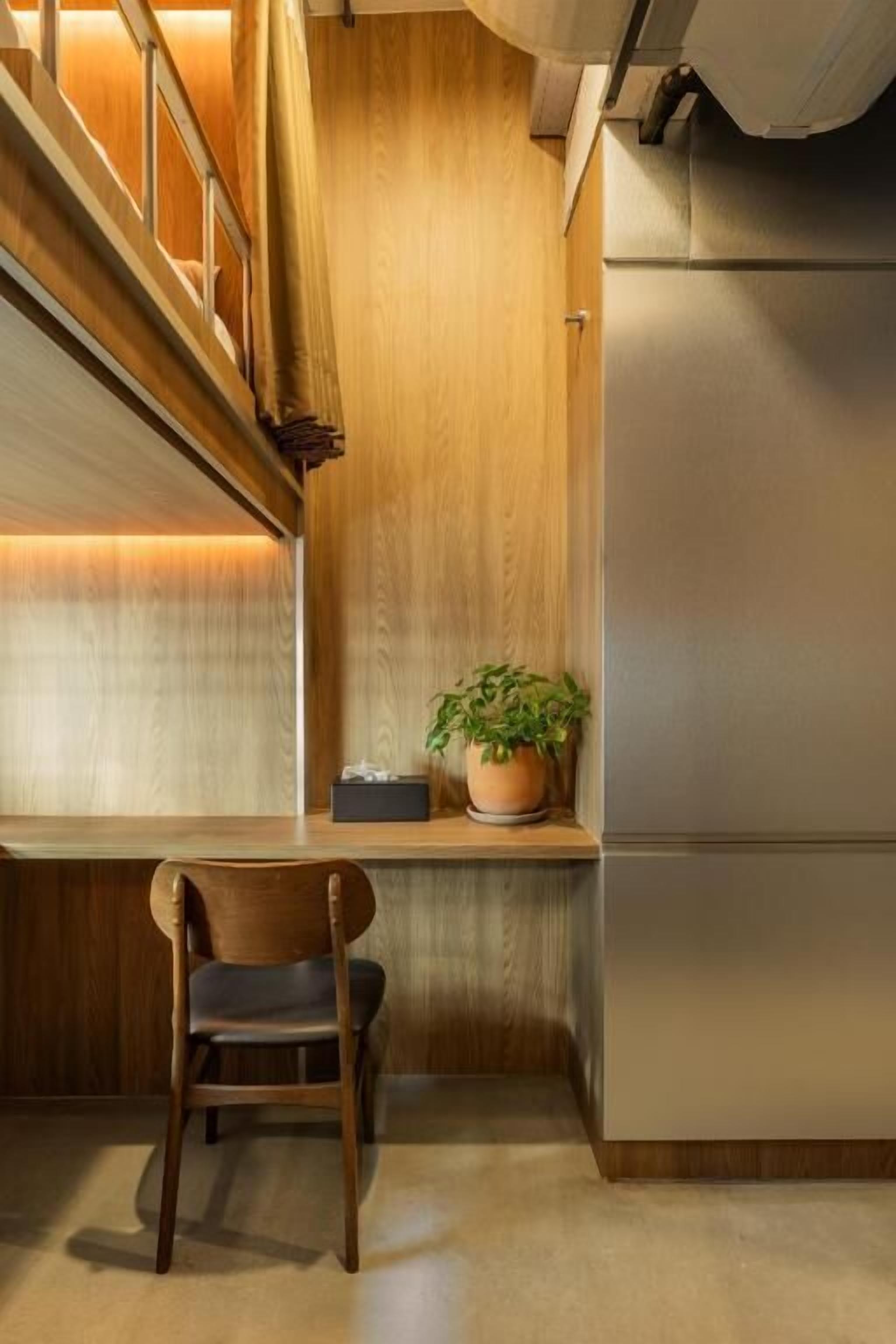 A corner of a room with a wooden desk, a chair, a potted plant, and a modern refrigerator.