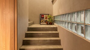 Eine Treppe mit einer Holztür links, einem gerahmten Bild mit Pflanzen an der Wand und einer Leuchte darüber.